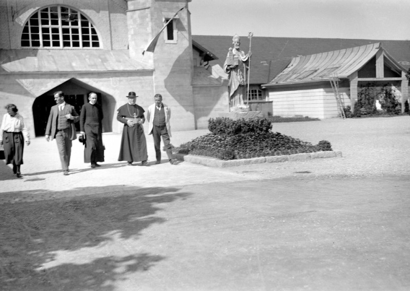 Historisches Foto: Gruppe vor Kirche mit Bischofsstatue. Schwarz-Weiß-Aufnahme.