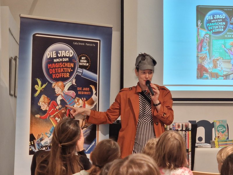 Autorin Cally Stronk präsentiert das Kinderbuch Die Jagd nach dem magischen Detektivkoffer bei einer Lesung vor Kindern.
