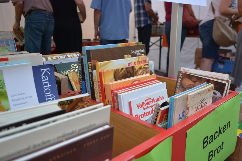 Bücherkiste mit Koch- und Backbüchern auf einem Flohmarkt, Fokus auf Brotbackbücher und Rezepte für Vollwertküche.